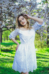 Beautiful blonde girl with blond hair in a dress on a background of spring blooming trees