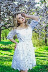 Beautiful blonde girl with blond hair in a dress on a background of spring blooming trees