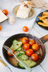 Roasted cherry tomatoes and cucumbers in frying pan.
