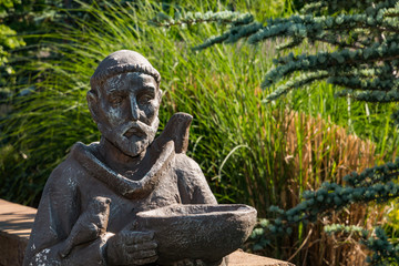Saint Stephens statue in a backyard against reeds and tree branches.