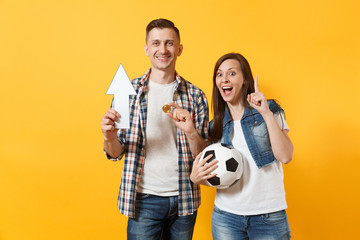 Couple, woman man, football fans holding bitcoin, metal golden coin, up arrow, soccer ball, cheer up support team isolated on yellow background. Sport bet, excitement ardor family lifestyle concept.
