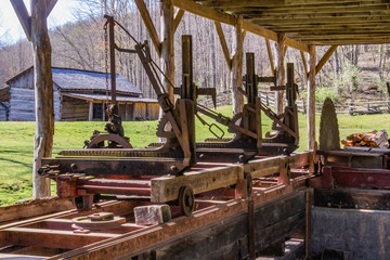 Old lumber mill or saw mill equipment with wheels, tracks and large blade.