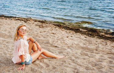 Beautiful young woman relaxing on the beach. She sits on the sand near the sea