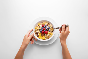 Young woman eating muesli cereal breakfast with berry fruit in a white bowl viewed directly from...