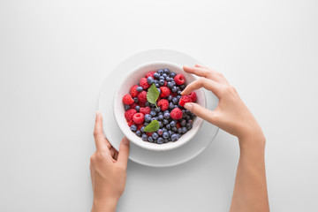 Young woman eating fresh berries (raspberry and blueberry) in a bowl viewed directly from above....