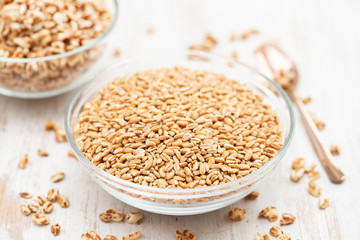 spelt in glass bowl on wooden background