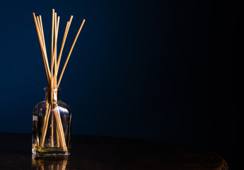 Reed diffusers in a small glass bottle on a table with a navy blue background - obrazy, fototapety, plakaty