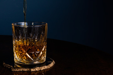 Whiskey being poured into a crystal tumbler on a dark wooden table