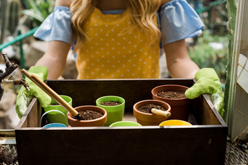 cropped shot of young woman in rubber gloves holding box with pots, soil and gardening tools