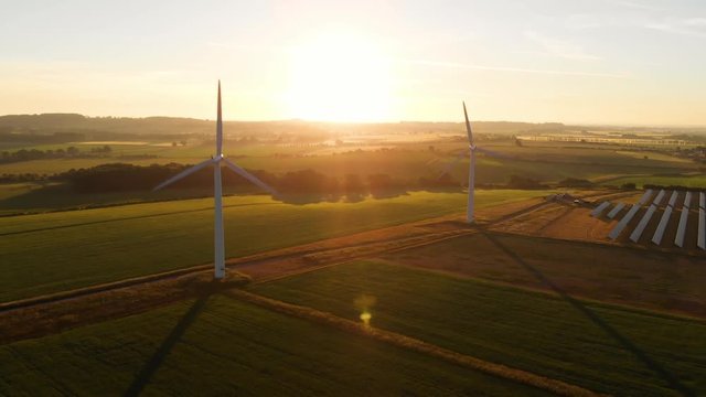 Aerial view of a wind farm and solar farm at sunrise with long shadows over farm land
