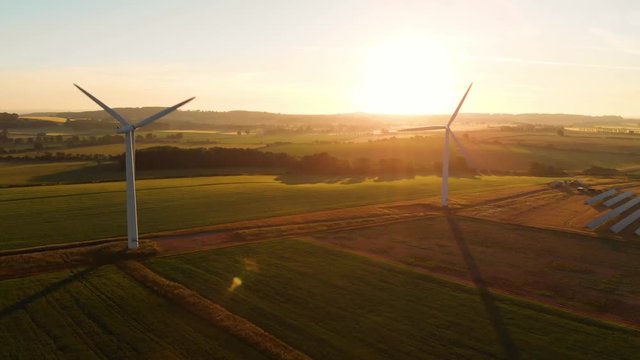 Aerial orbit around a wind farm and solar farm at sunrise with long shadows over farm land