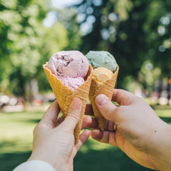 first-person point of view. two hands holding ice cream with city park on background