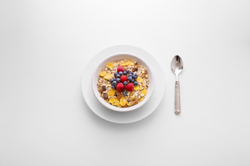 Muesli cereal breakfast with berry fruit in a white bowl with a spoon on the side viewed directly from above. Fresh rich in fiber granola dish viewed from above. Top view. Copy space