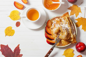 pancakes with tea  and plums on white wooden table