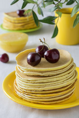 A stack of pancakes with cherries in the foreground, honey, a cup of tea and a green line in the background