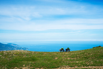 Fototapeta na wymiar Two people sit on tourist chairs on the mountain and look at the sea. Aerial panoramic view of the city of Yalta in Crimea, Russia. Ayu-Dag or Bear Mountain in the background. 