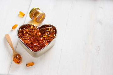 Fish oil capsules in a heart shape plate on white wooden background and texture, vitamin D supplement, selective focus