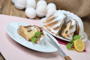 Cut of bundt cake sprinkled with sugar, lemon, melissa, milk, eggs and butter
