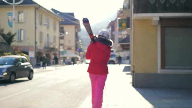 Woman Walking Near Houses Holding Her Alpine Ski On The Shoulder Before Skiing