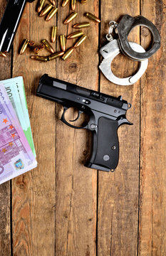 View from above of 9mm handgun pistol - handgun, handcuffs, bullets, euro banknotes and magazine on old wooden table - vertical photo