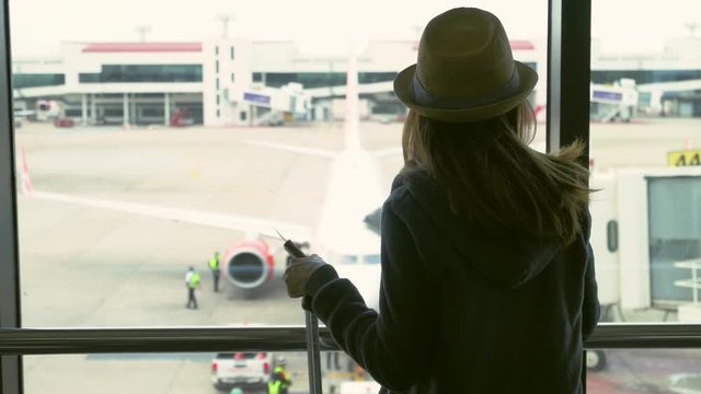 Young woman traveler with luggage holding passport looking at the airplane at the airport, Travel concept