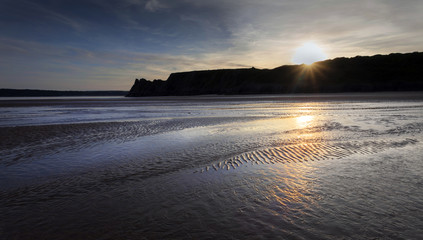 Gower sunset and wet sand at The Great Tor and Three Cliffs Bay, Swansea, Wales, UK
