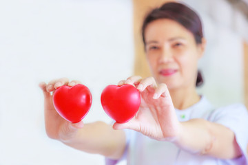 Red heart held by smiling female nurse's hand, representing giving effort high quality service mind to patient. Professional, Specialist in white uniform concept