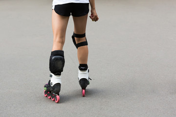 Fototapeta premium Close up beautiful slim legs of young girl in short shorts wearing roller skating in a sunny day in summer in the park. Knee protectors