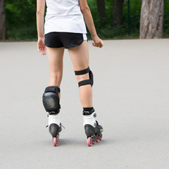 Close up beautiful slim legs of young girl in short shorts wearing roller skating in a sunny day in summer in the park. Knee protectors