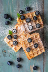 Waffles with blueberries on a rustic green and blue background. View from above.