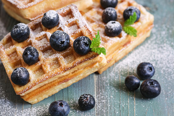 Homemade Belgian waffles with blueberries are sprinkled with powdered sugar on a green wooden rustic background. Selective focus. Close-up