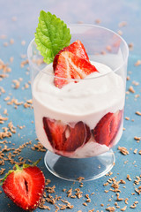 Yogurt with fresh strawberries in a glass on a blue background. Selective focus. Summer dessert with strawberries.