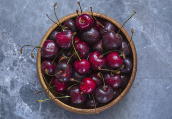 Ripe cherry in a wooden bowl against a background of blue marble with drops of water

