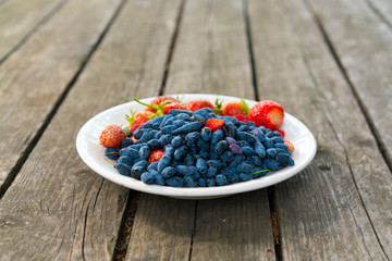 Summer berries - strawberries and honeysuckle on a wooden base in sunny weather. Still life, with...