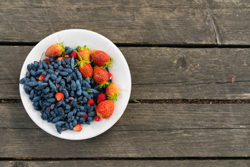 Summer berries - strawberries and honeysuckle on a wooden base in sunny weather. Still life, with...