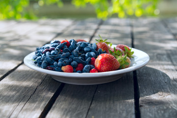 Summer berries - strawberries and honeysuckle on a wooden base in sunny weather. Still life, with fruit assorted platter with lot ripe appetizing strawberry and honeysuckle view closeup