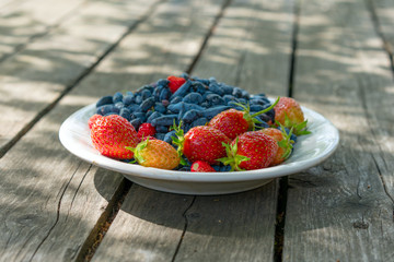 Summer berries - strawberries and honeysuckle on a wooden base in sunny weather. Still life, with...