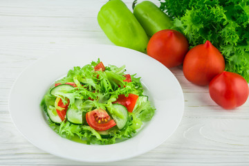 light summer salad of tomatoes, cucumbers and lettuce leaves, on a wooden background