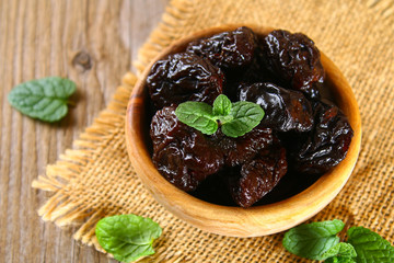 Prunes with mint leaves in a bowl on an old wooden table.
