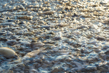 pebble stones on the sea beach, the rolling waves of the sea with foam