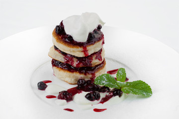 Tasty breakfast. Fritters with sour cream and blueberry jam.
They lie on a white dish and are decorated with a mint leaf.