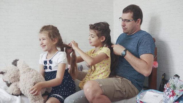 Dad and two little daughters at home. father spends time with children. father makes pigtails for his daughter