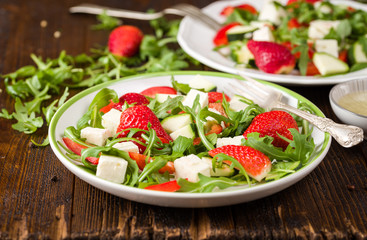 Fresh vegetable strawberry salad on white plate on natural rustic desk.