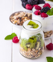 White yogurt with muesli in glass bowl with pieces of kiwi on top.