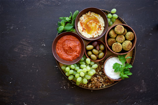 Meze platter with muhammara dip, hummus dip, yogurt dip and other snacks. Middle East cuisine. Top view, dark brown background
