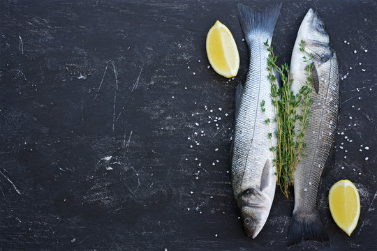 Raw uncooked seabass with thyme and lemon. Black shabby background
