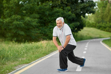 Active senior man exercising on fresh air. Morning pushing-up on city park's race track. Grandfather having fit body, healthy lifestyle.Wearing white polo shirt, balck trousers, sport sneakers.