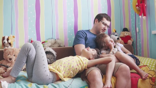 the young father and two little daughters play with soft toys, smile and laugh. father enjoys time with children