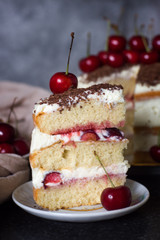 Sponge cake with creamy cream with cherries and chocolate. A piece of cake close-up on the background of the rest of the cake in a soft focus.