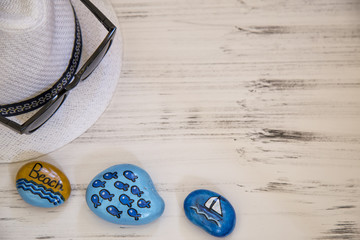 Colorful painted stones with hat and glasses on wooden background . summer concept .